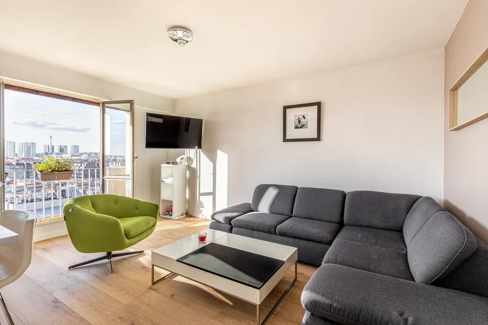A bright living room with gray seating and a green accent chair beside a balcony.