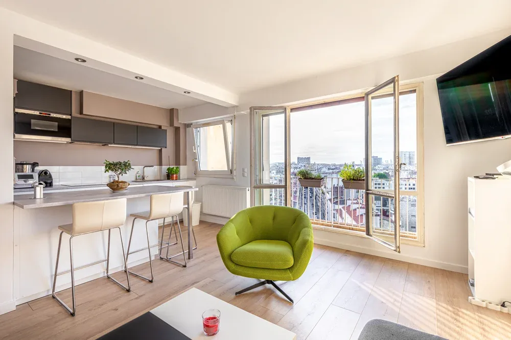 A bright open-plan kitchen and living area with a green armchair beside the balcony doors.