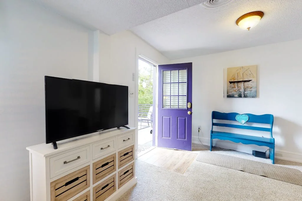 A bright living room with a television, a purple door, and blue seating.