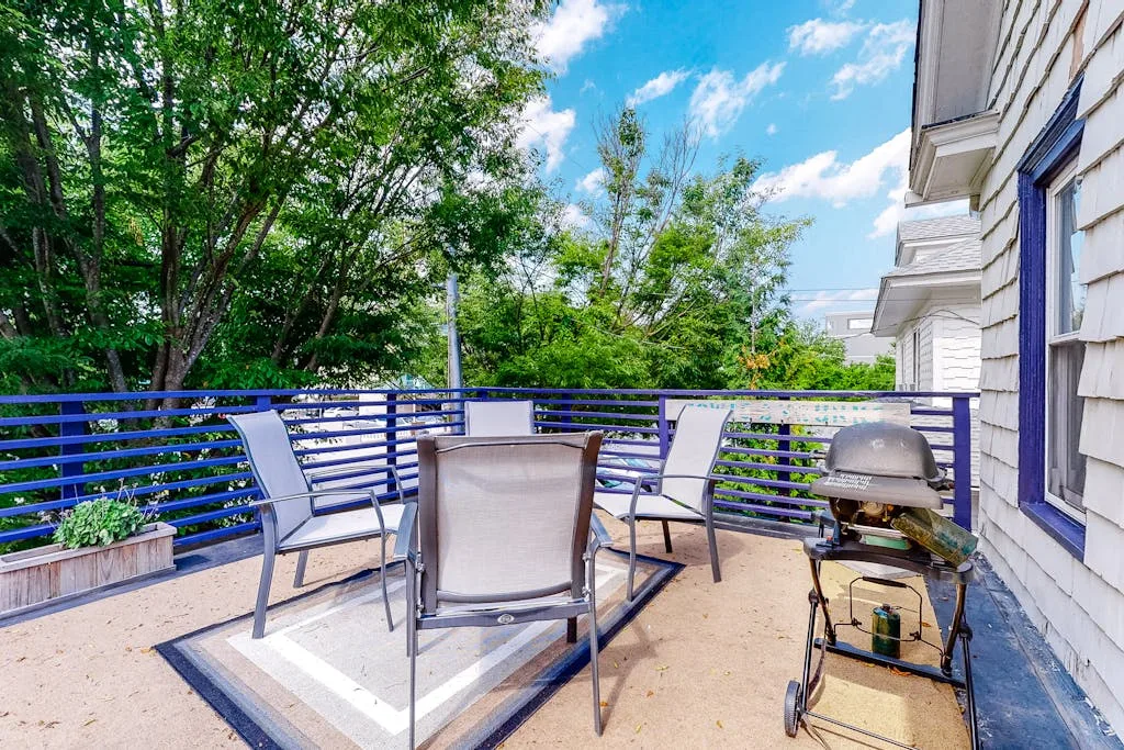 An outdoor patio has seating, a blue railing, and a barbecue grill.