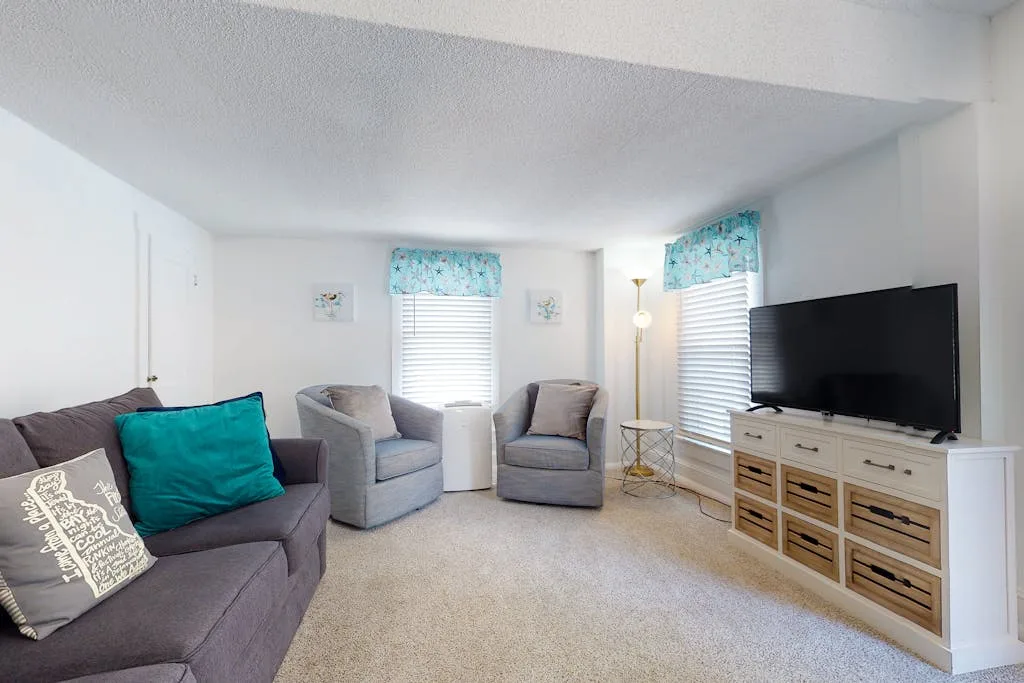A bright living room with seating, curtained windows, and a television.