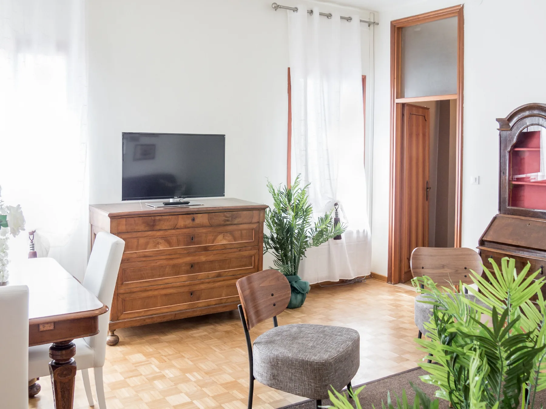 A bright living room with a television on a wooden dresser and plants.