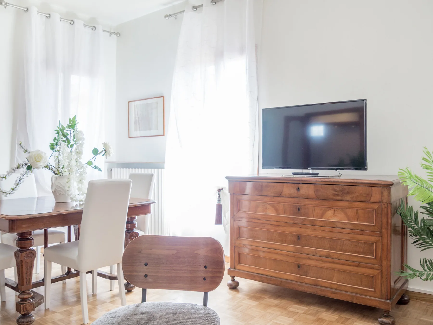 A bright dining and living area with a wooden table and television on a dresser.