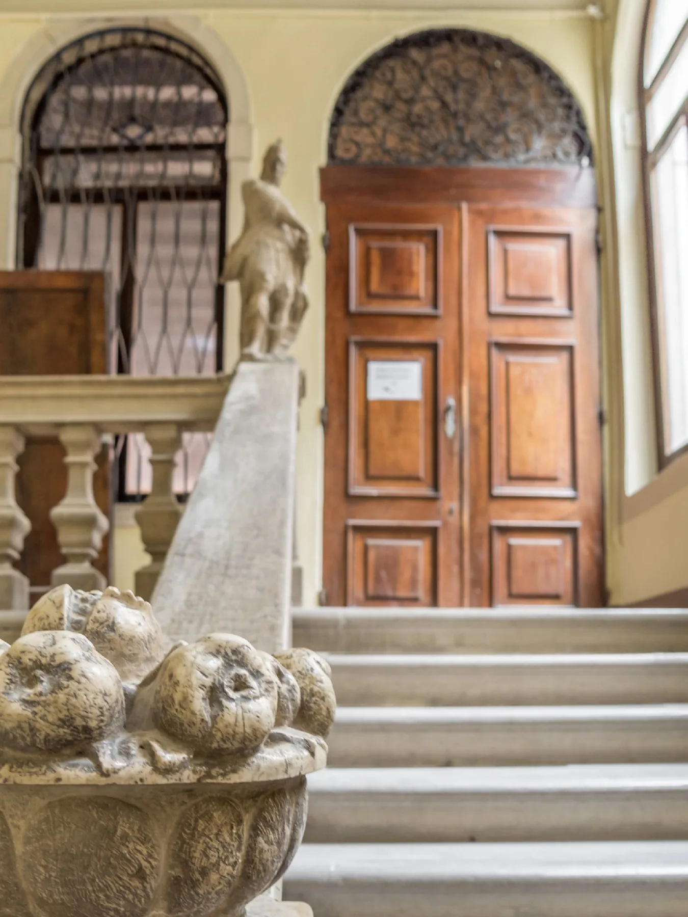 An ornate wooden doorway opens onto a stone stairway, with a carved fountain in the foreground.