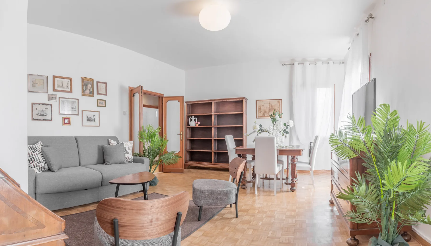 A bright living and dining room with a gray seating area and wooden shelving.