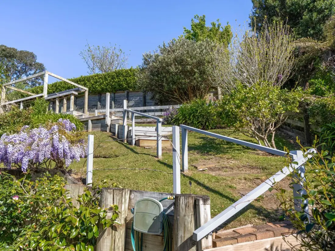 A garden with stairs leading up to a fenced area at Harbour house - Whangamata Holiday Home