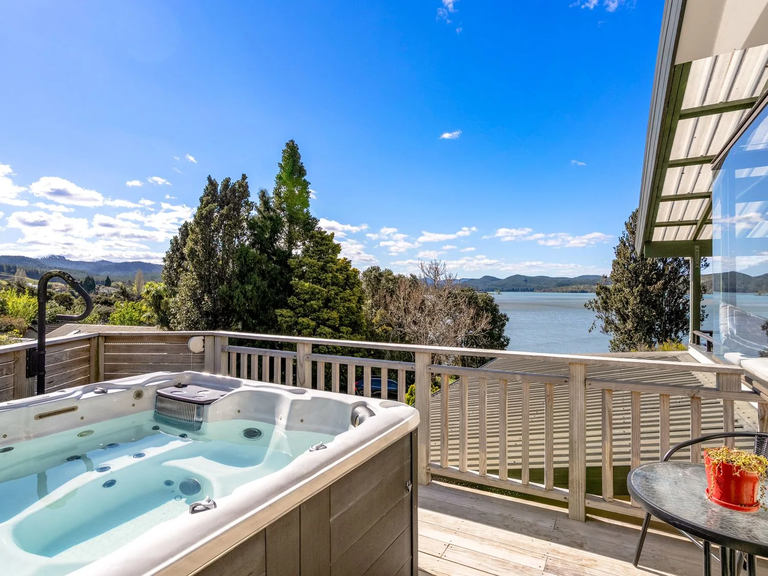 A deck overlooks the water, with a hot tub and small table nearby.