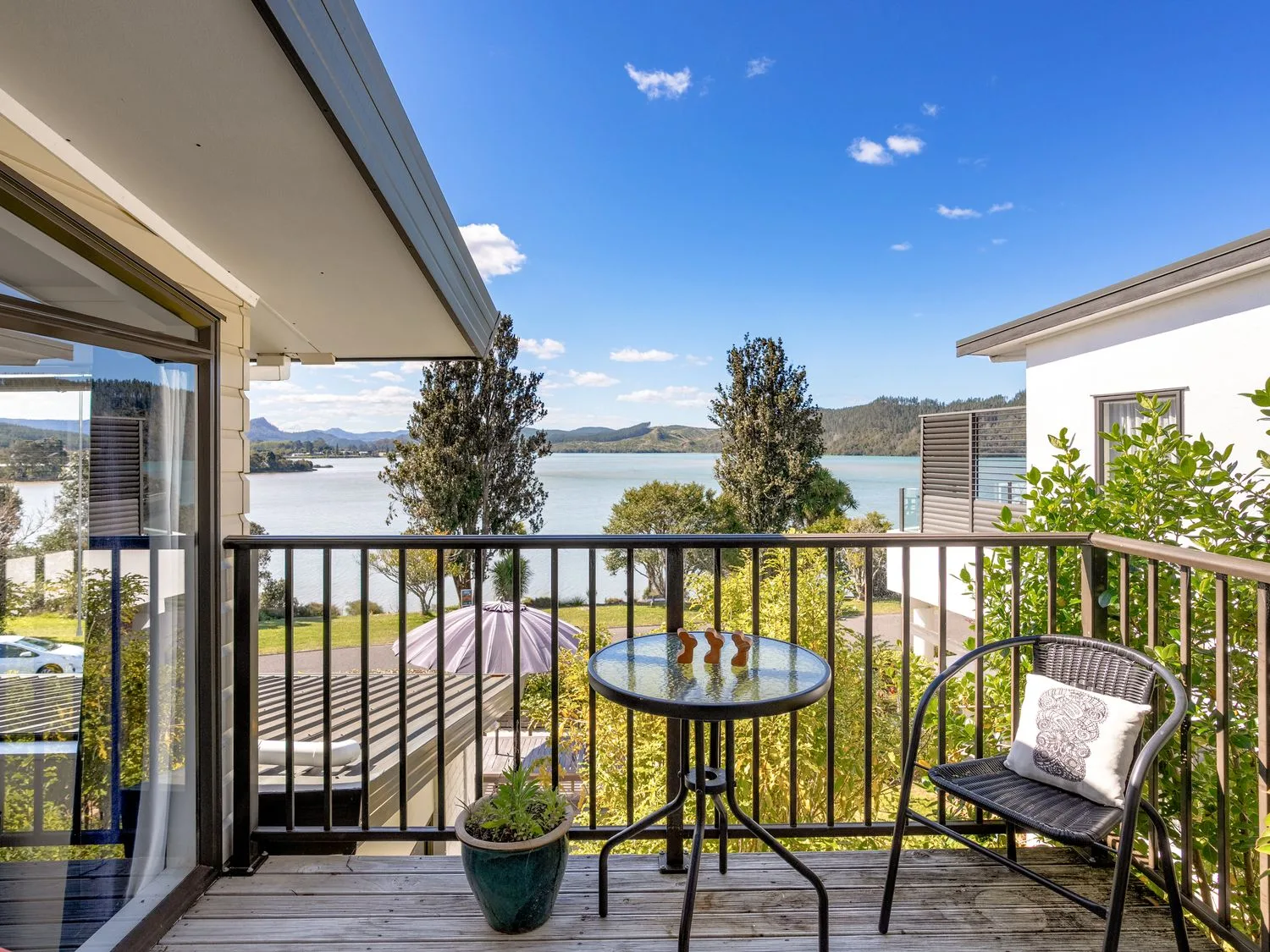 An outdoor area with a table and chair overlooking the water at Harbour house - Whangamata Holiday Home
