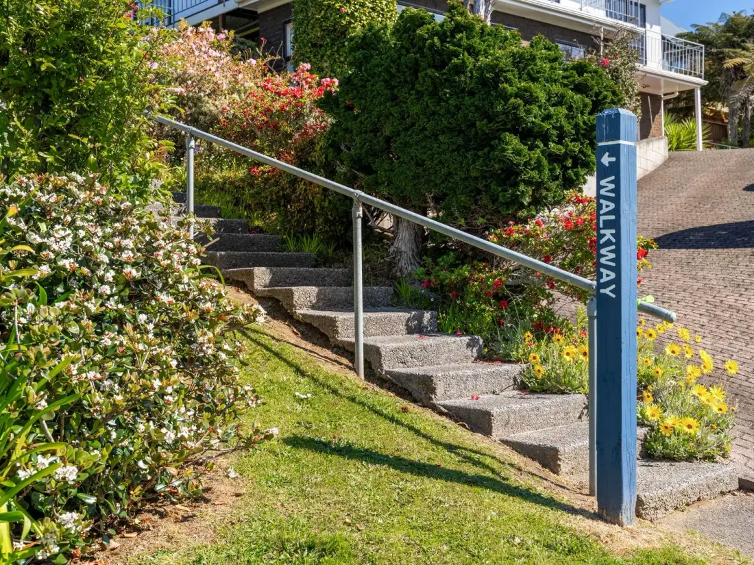 A landscaped outdoor walkway with concrete steps, a handrail, and flowering shrubs.