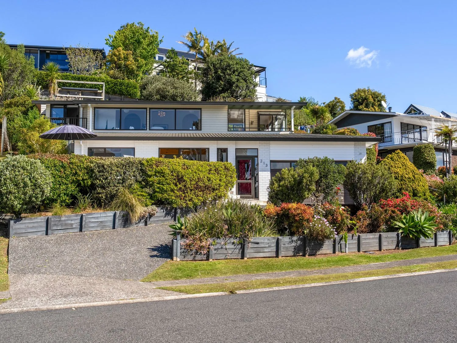 A modern house stands behind a landscaped front garden and driveway.