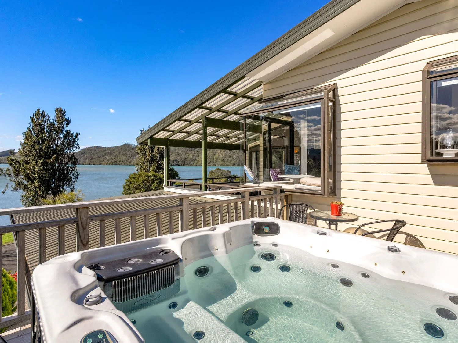 An outdoor patio with a hot tub and chairs at Harbour house - Whangamata Holiday Home