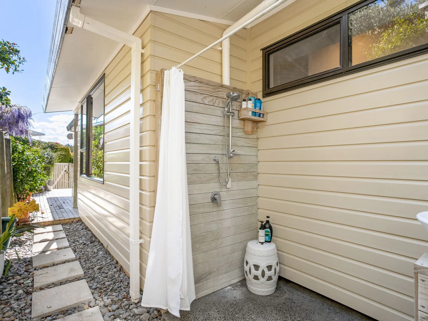 An outdoor shower beside a light-colored exterior wall and paved walkway.