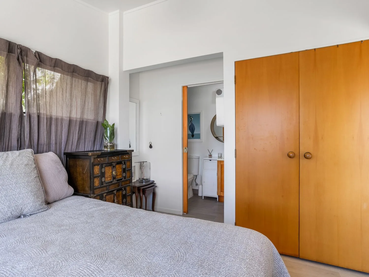 A bedroom with a bed, curtained window, and bathroom visible through the doorway.
