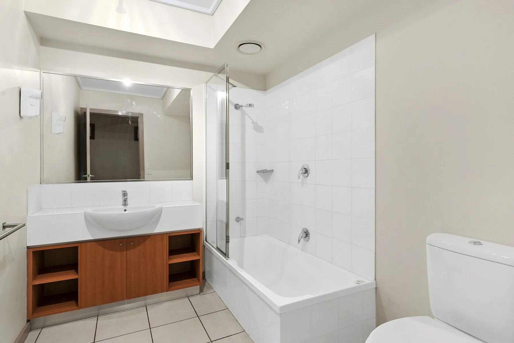 Un baño alicatado con bañera, lavabo y mueble de madera.