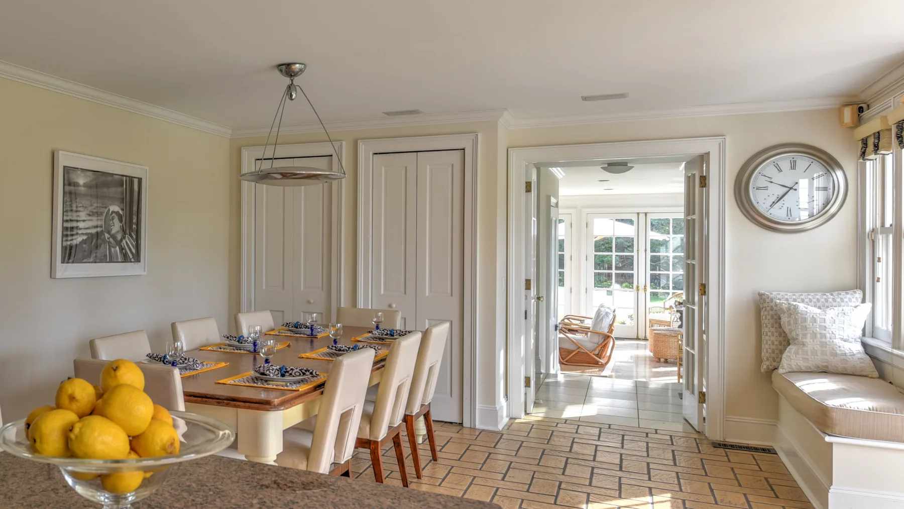 A dining area with a set table and a bright adjoining sitting room.