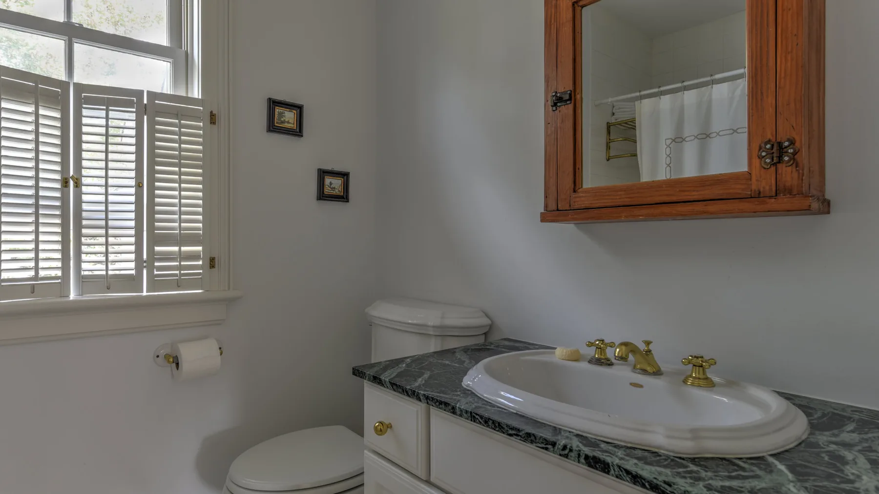 A bathroom vanity with a sink and mirrored cabinet sits beside a shuttered window.