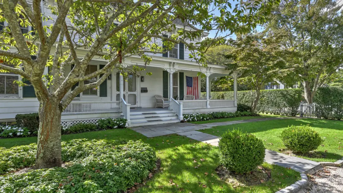 A white house with a covered porch, front steps, and a landscaped garden.