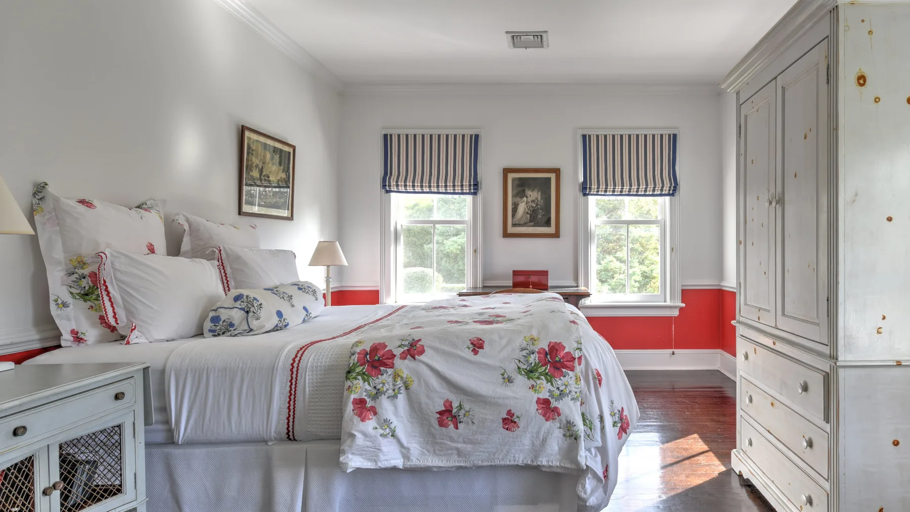 A bright bedroom with floral bedding and two windows.