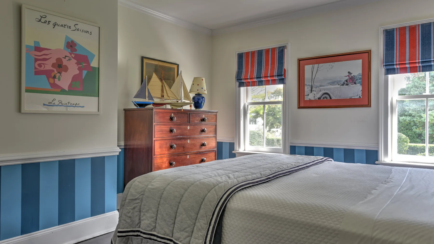 A bedroom with a bed, wooden dresser, and striped window shades.
