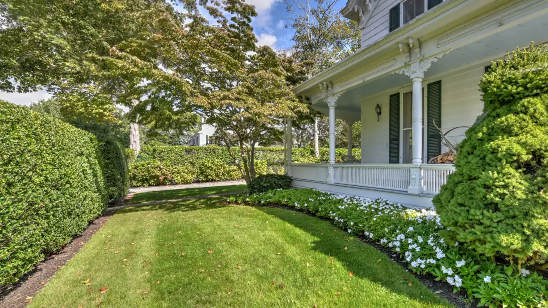 A landscaped garden beside a white house with a covered porch.
