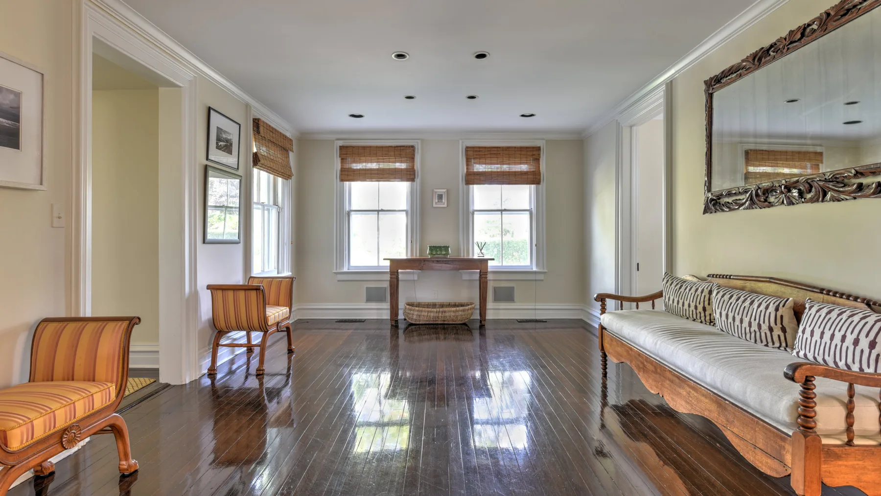 A bright living room with wooden seating and windows overlooking a glossy floor.