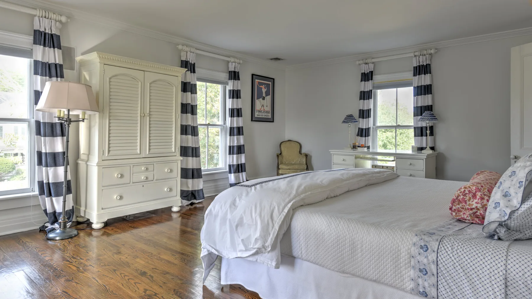A bright bedroom with a bed, a dresser, and striped window curtains.