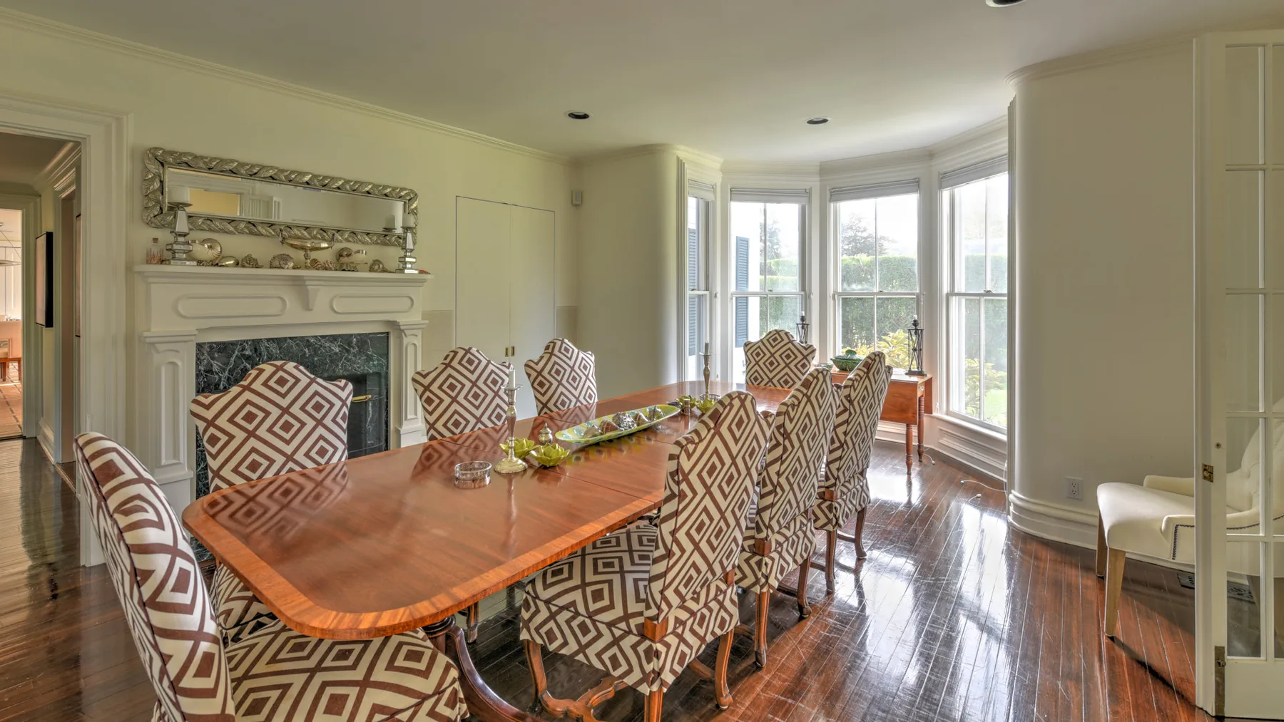 A dining room with a long wooden table and patterned upholstered seating.
