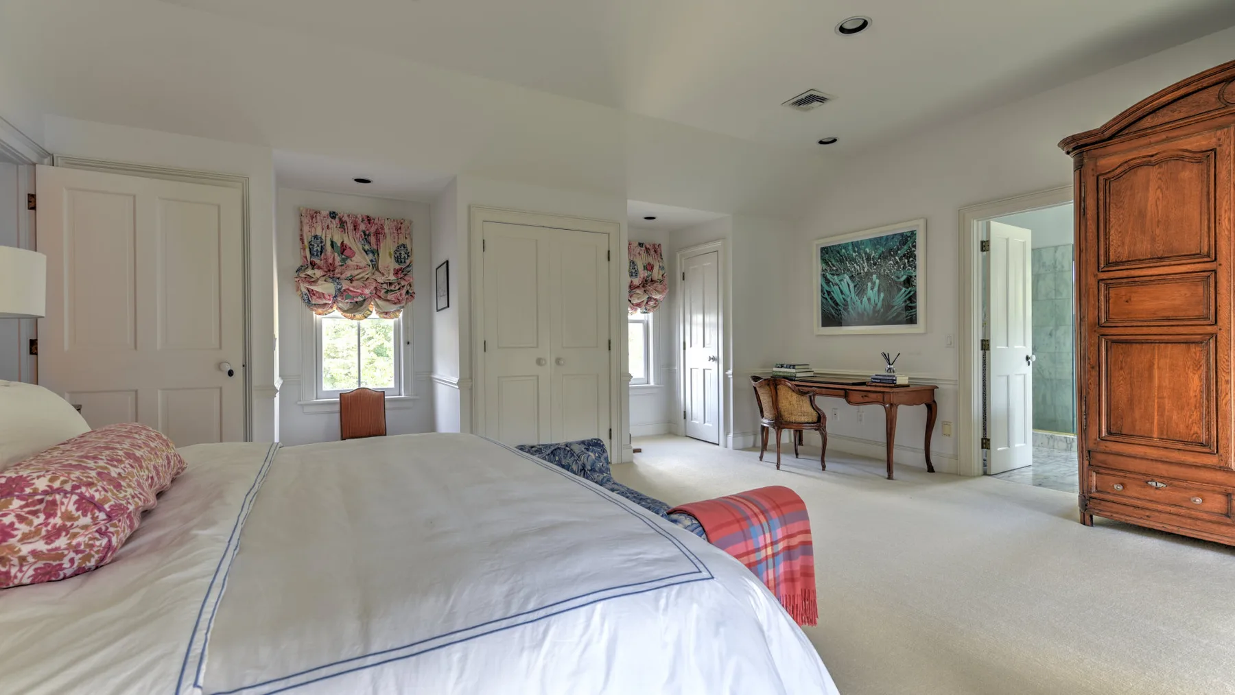 A bedroom with a large bed, floral window coverings, and a wooden cabinet.