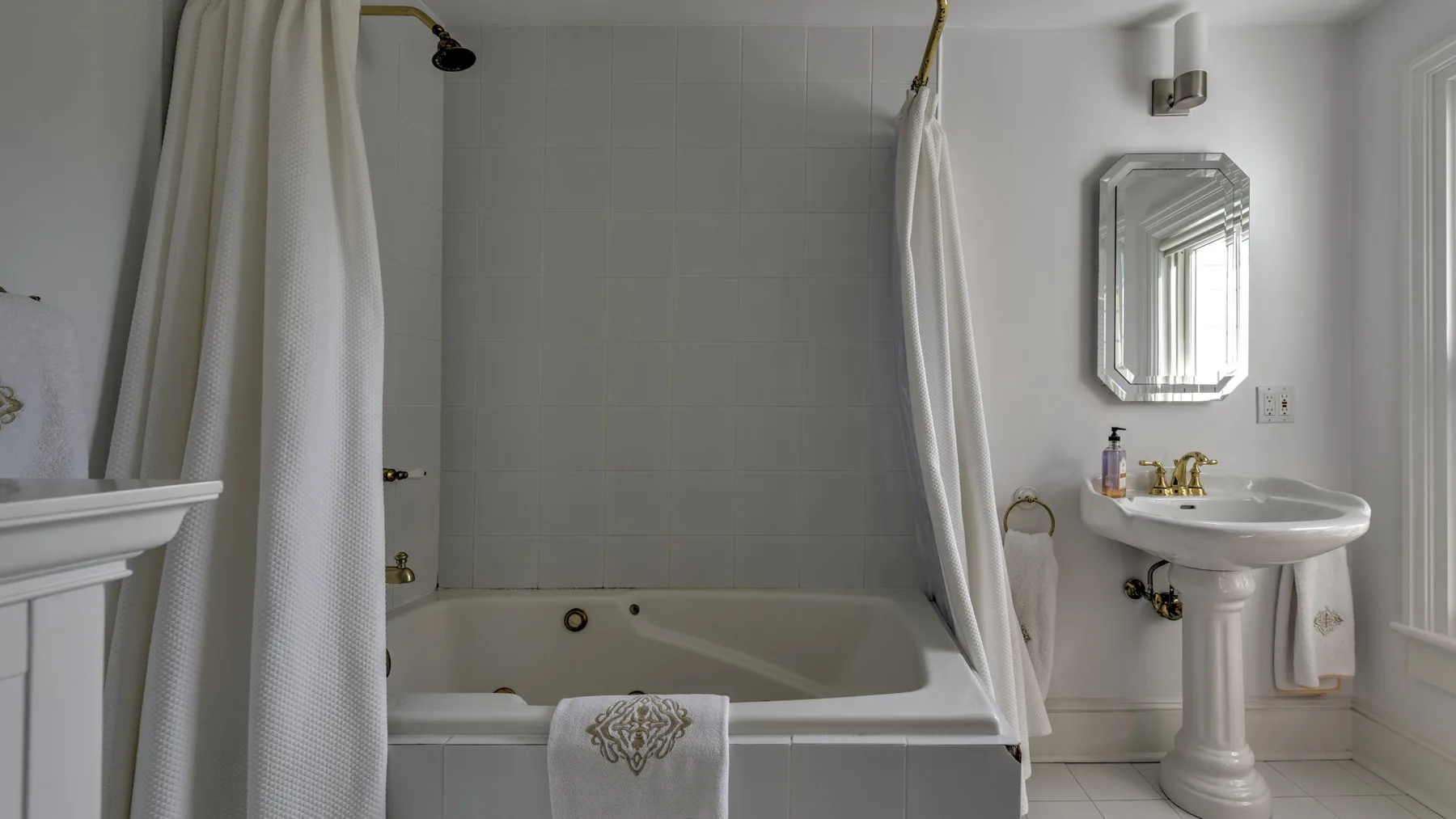 A bathroom with a bathtub, shower curtain, and pedestal sink.