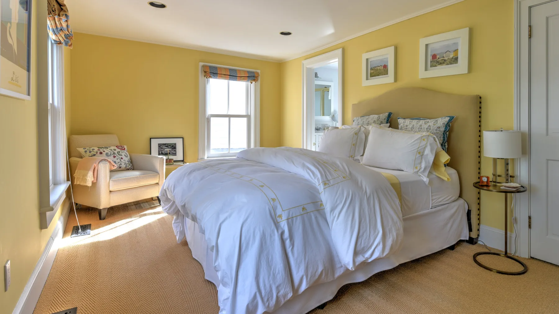 A bedroom with a bed, a small seating area, and yellow walls.
