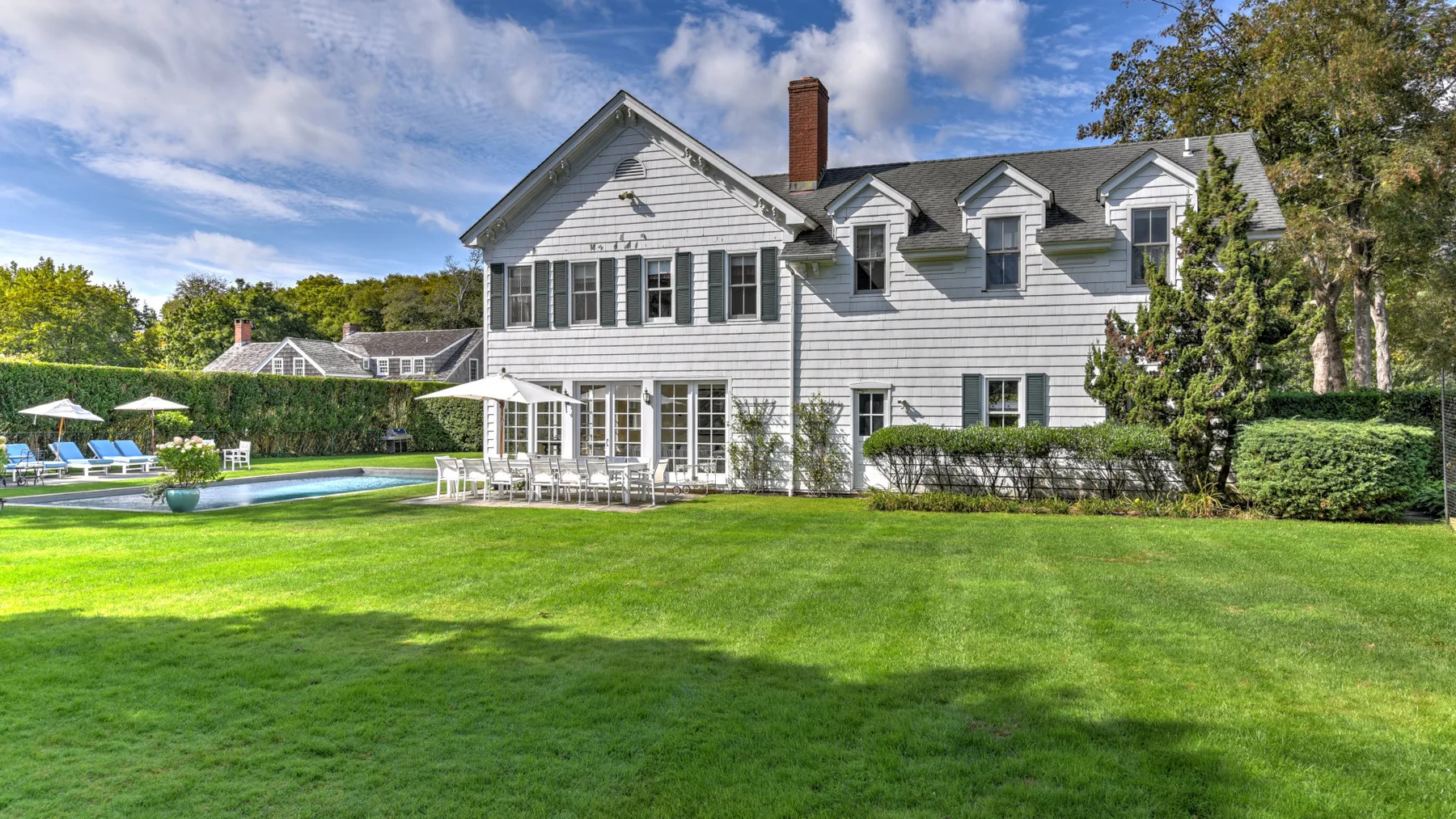 A large white house overlooks a green lawn and outdoor swimming pool.