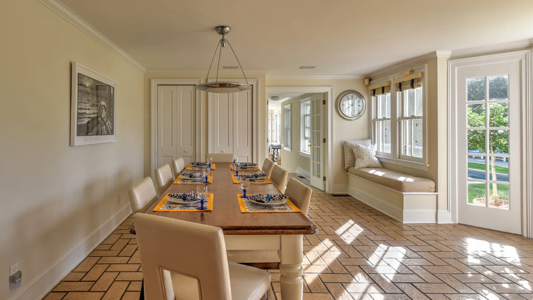 A bright dining room with a long table beside large windows.