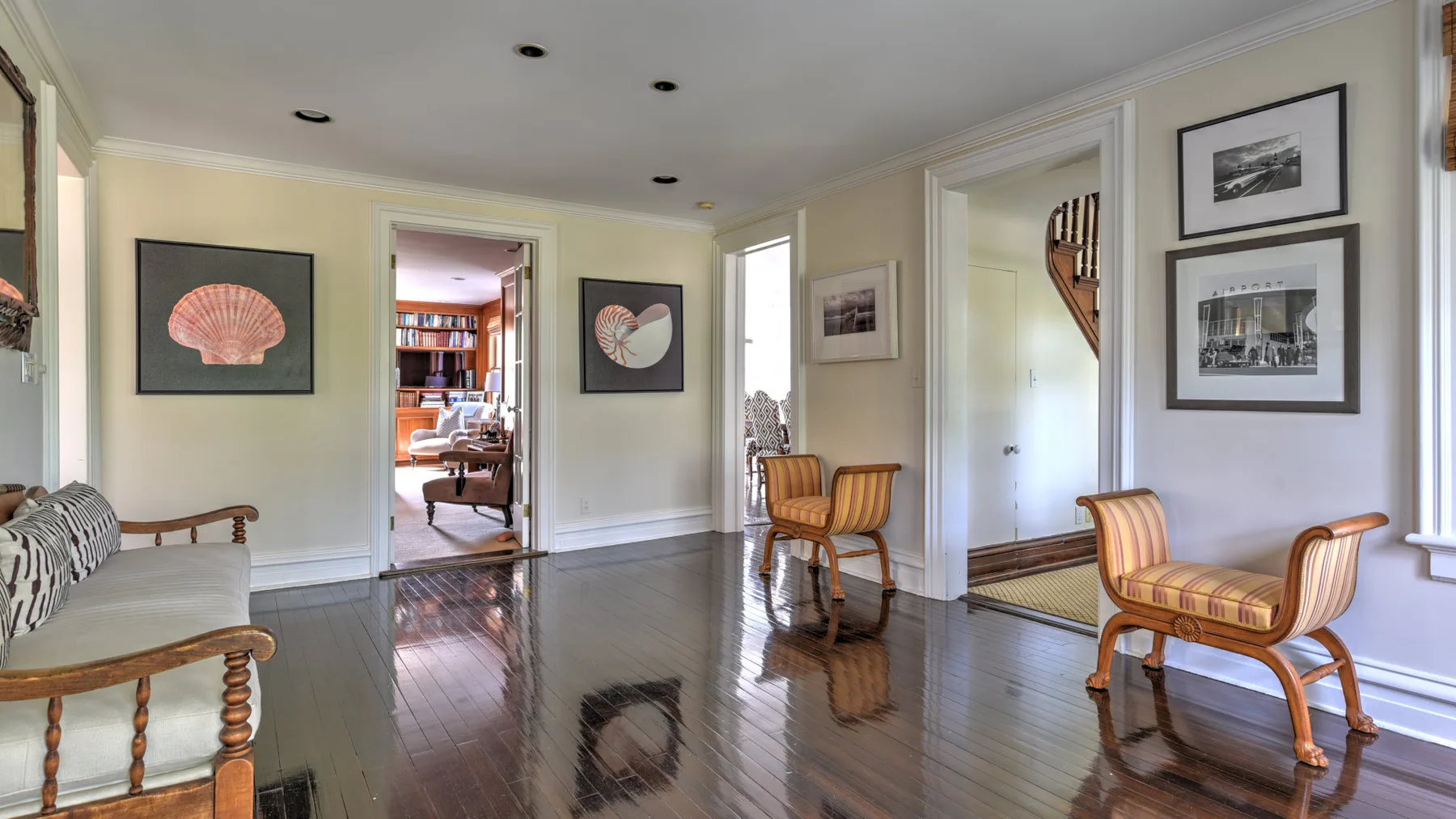 A bright sitting room with wood flooring, framed artwork, and striped seating.