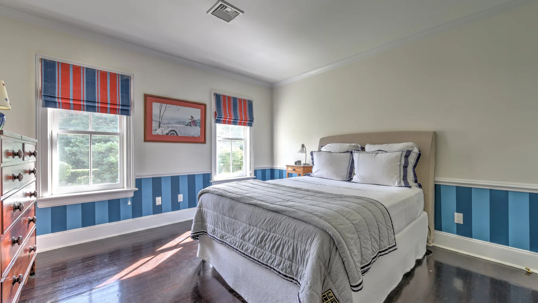 A bedroom with a bed, striped window shades, and blue wall paneling.
