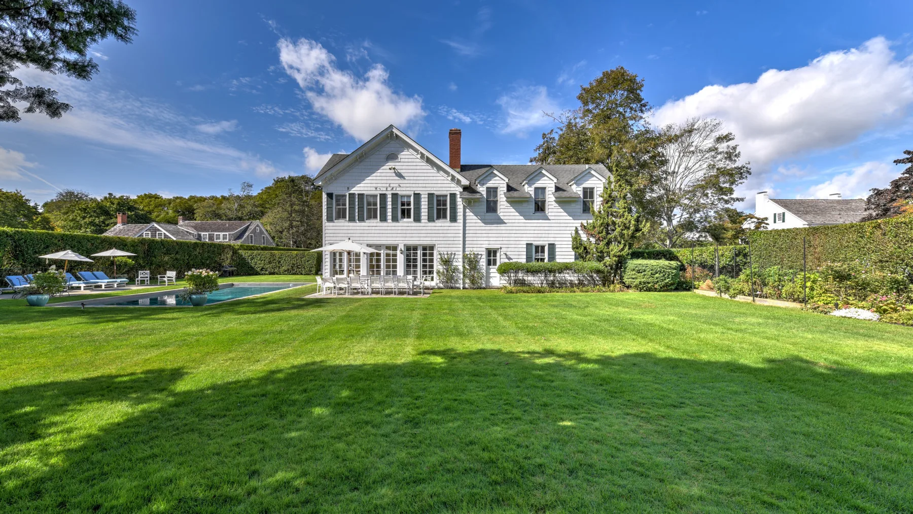 A white house overlooks a broad green lawn, with a swimming pool nearby.