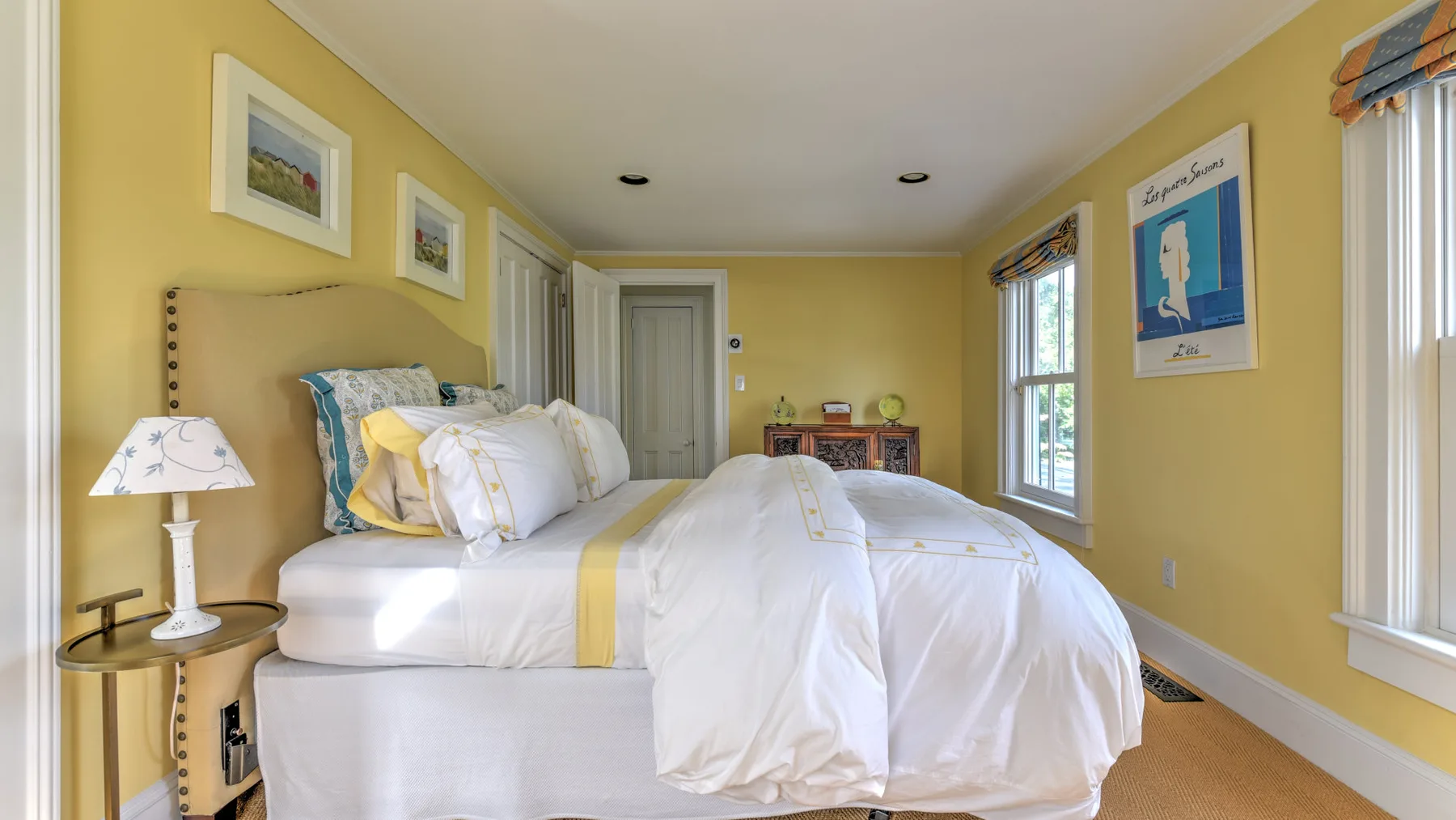 A bedroom with a large bed, white bedding, and yellow walls.