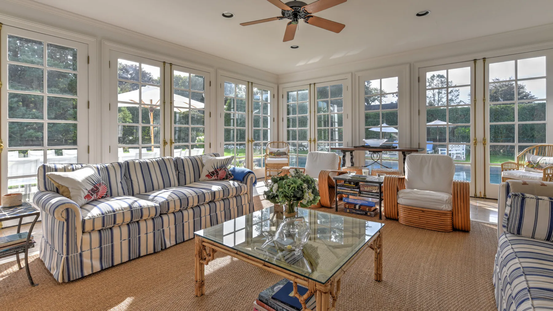 A bright sunroom with striped seating and a glass coffee table.
