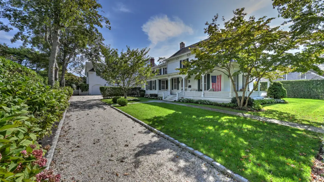 A white house stands beside a gravel driveway and a green lawn.