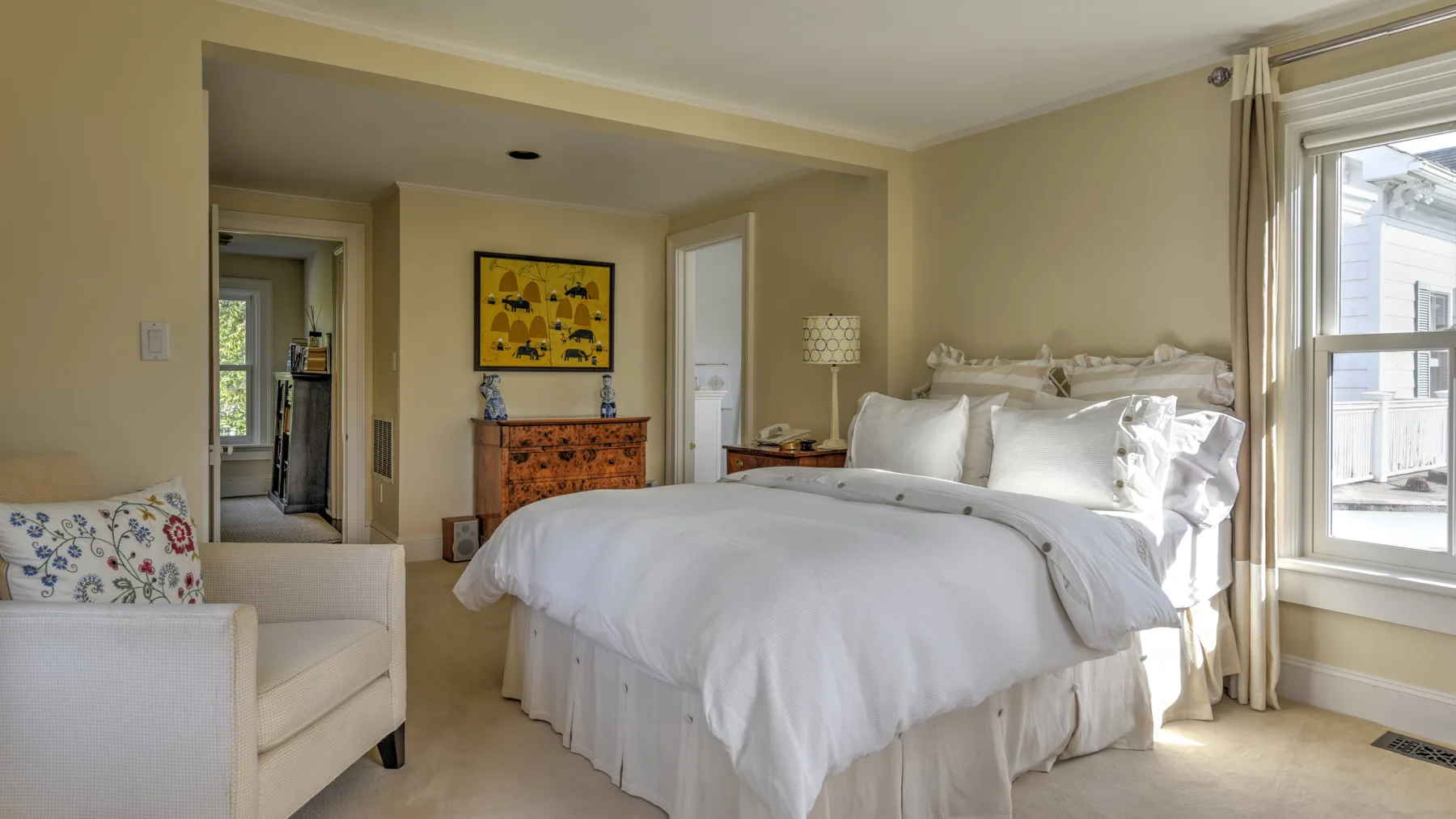 A bright bedroom with a large bed, a cushioned chair, and a sunny window.