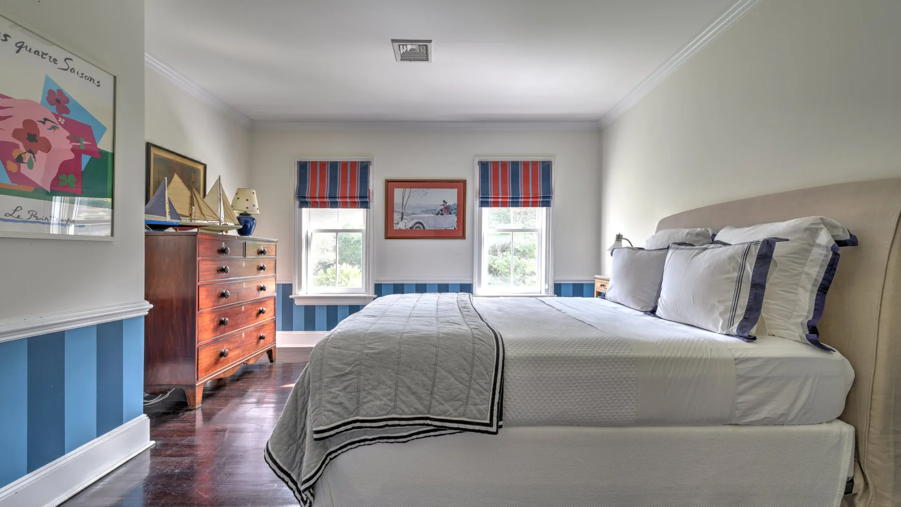A bedroom with a neatly made bed and two windows.
