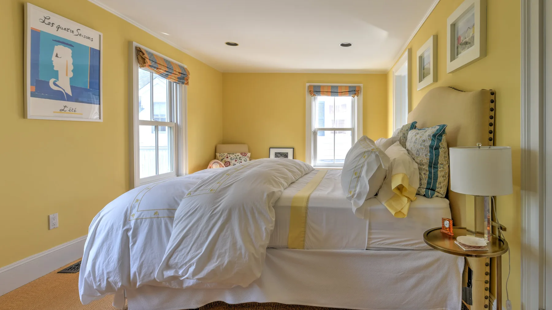 A bedroom with a bed dressed in white linens and yellow walls.