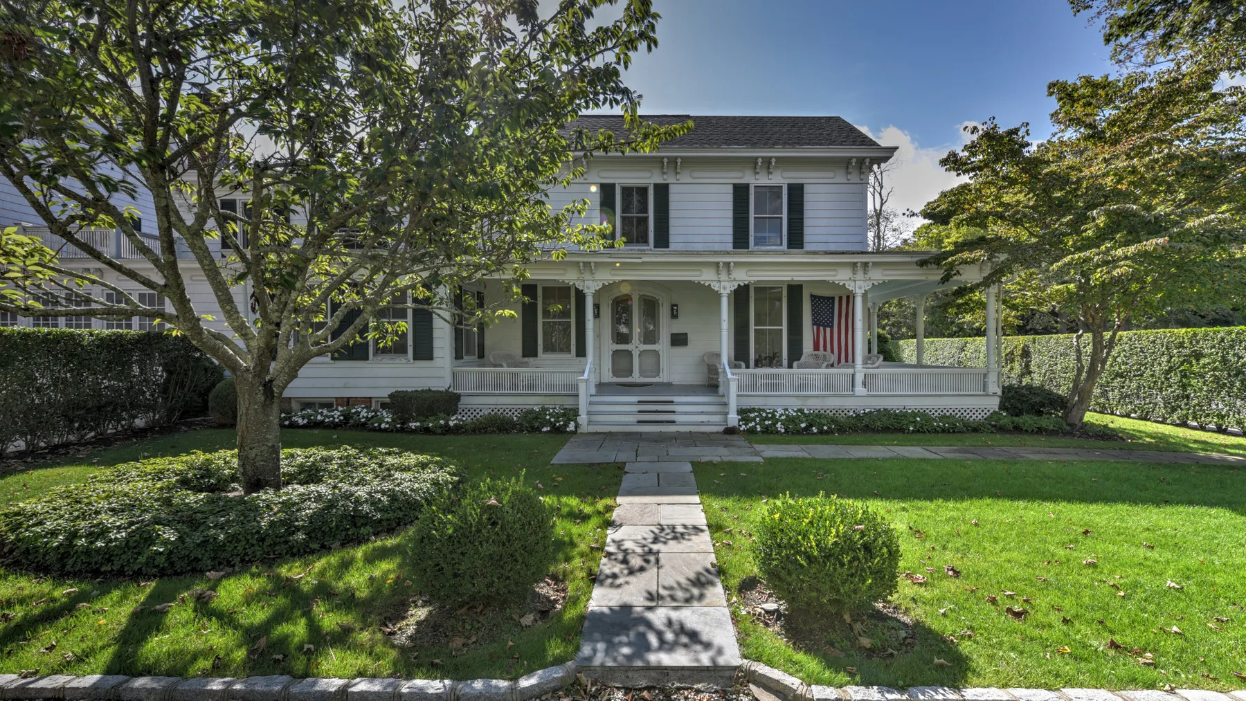 A white two-story house with a covered porch and a walkway through the front lawn.