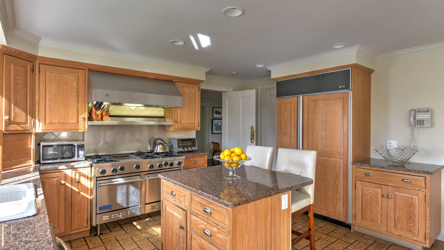 A kitchen with wooden cabinets and a central island topped with a bowl of fruit.