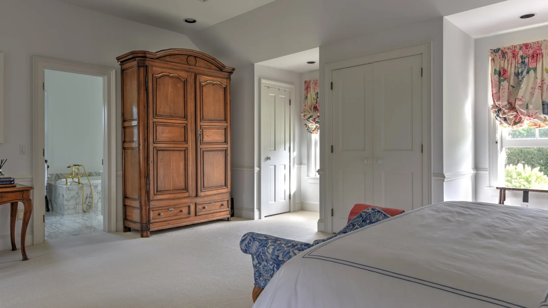 A bright bedroom with a large wooden wardrobe and a bed.