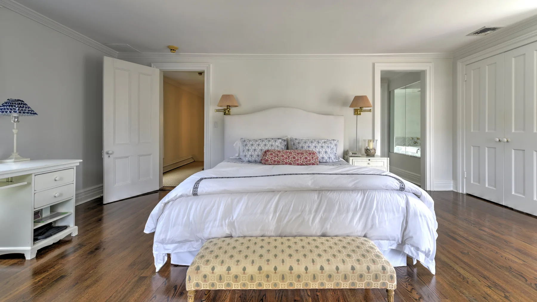 A bright bedroom with a large bed, bedside lamps, and a cushioned bench.