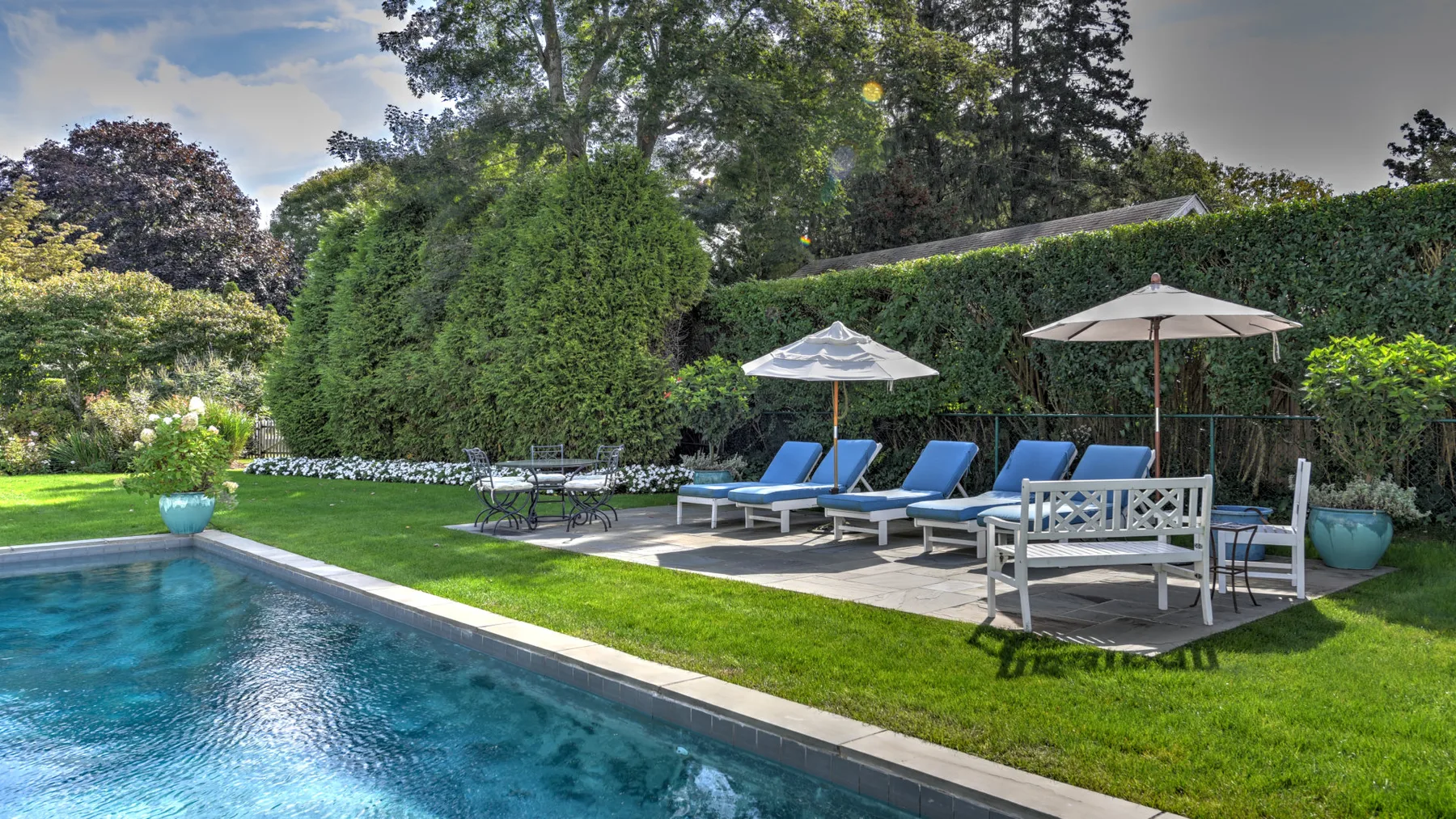 An outdoor swimming pool beside a grassy patio with seating and umbrellas.