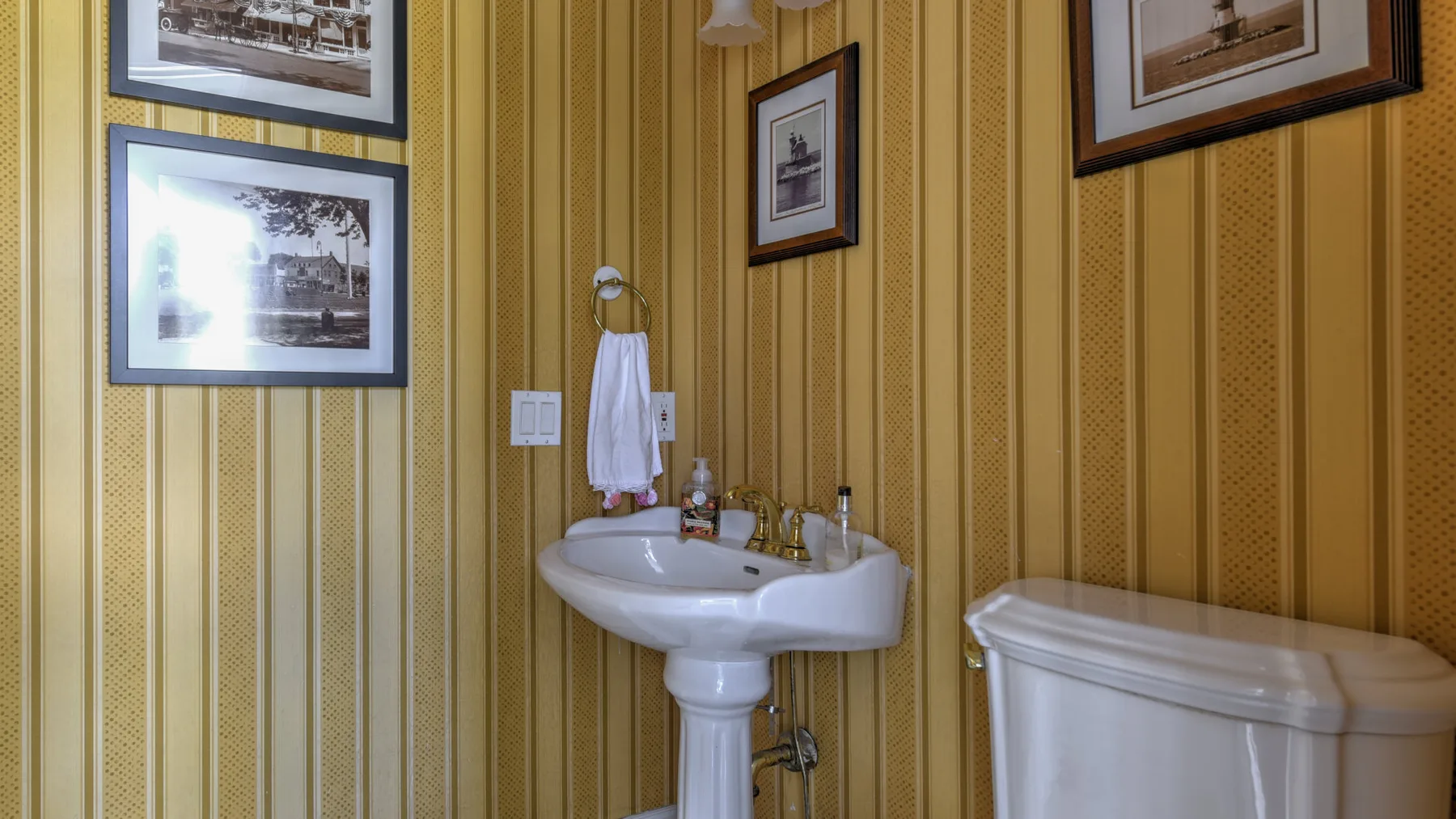 A bathroom with a pedestal sink and framed pictures on striped walls.