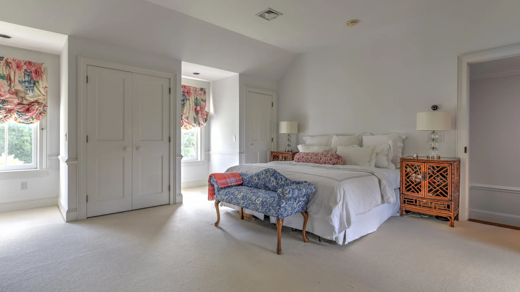 A bright bedroom with a large bed and a patterned bench at its foot.