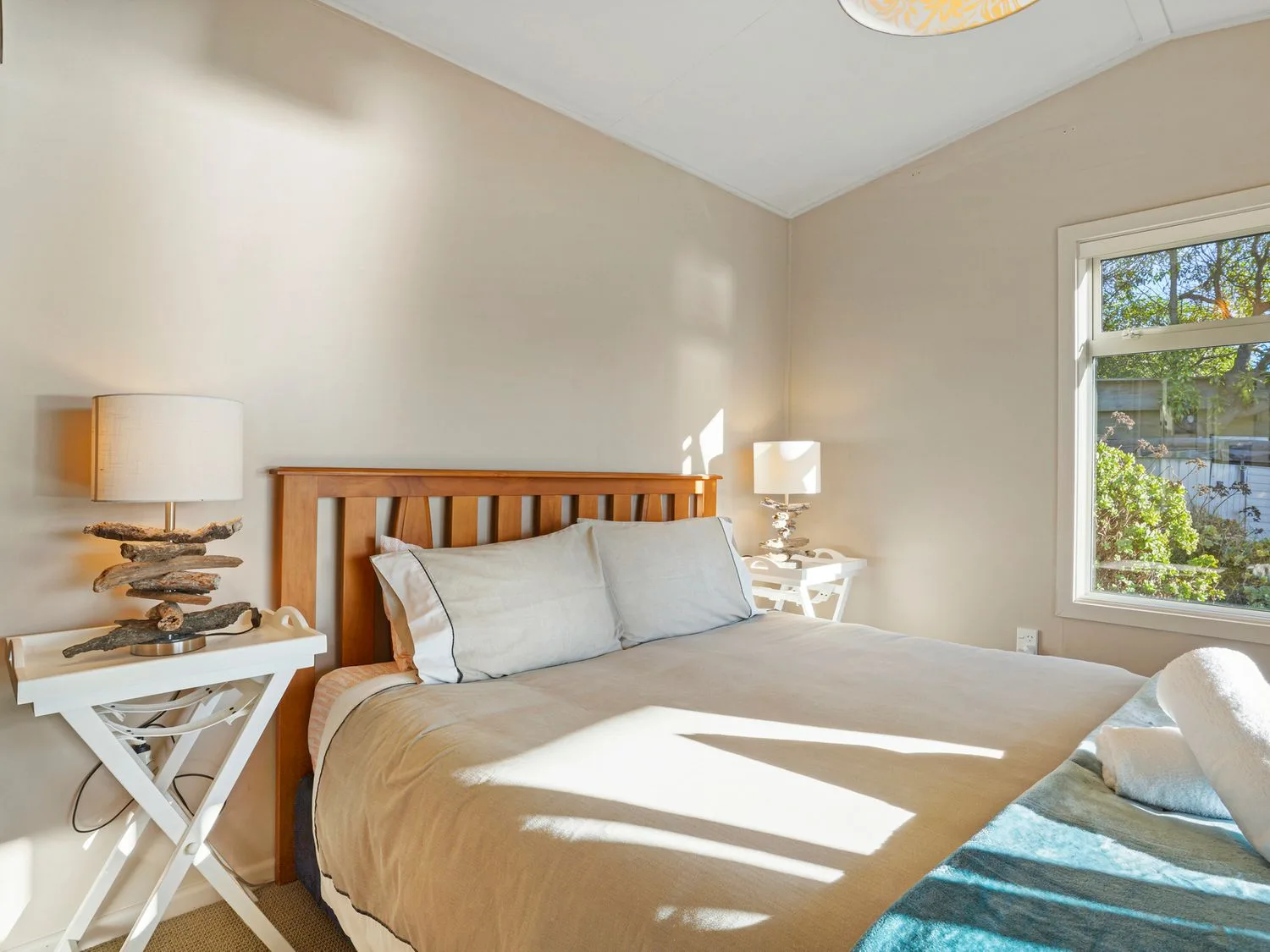 Un dormitorio con una cama de madera y mesitas blancas junto a una ventana.