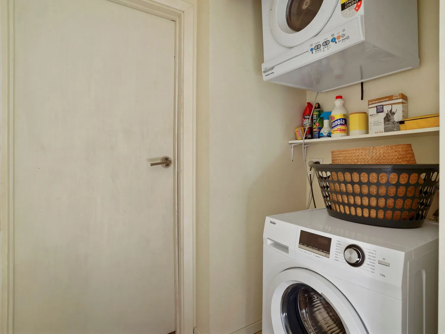 Un lavadero con una lavadora y una secadora apiladas, una repisa con productos de limpieza y una cesta para la ropa en Kaioruru View, en Diamond Harbour